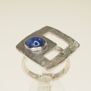 Anello con testa quadrata con effetto fuso montata a rombo e incastonato uno zaffiro cabochon ct 1,84 e zirconi  taglia 15